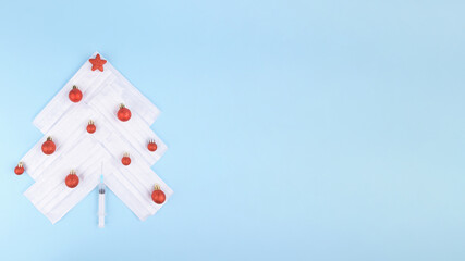 Alternative Christmas tree of medical disposable protective face masks forming a Christmas tree with red balls on a blue background. Christmas and Happy New Year concept during pandemic of coronavirus