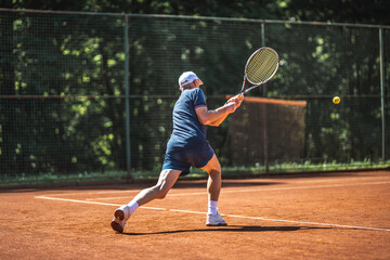 Active senior Caucasian man in sportswear playing tennis, steps forward and hits a ball