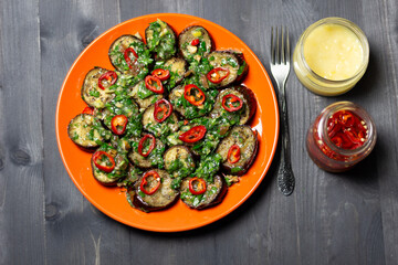 Eggplant salad with herbs and spices on red plate on black wooden background