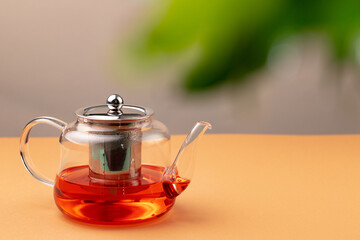 Glass teapot with black tea on background of blurred foliage
