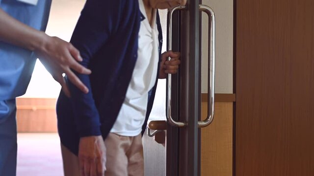 病院を歩く高齢女性を介助する看護師