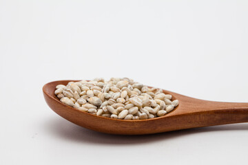 Wooden spoon with unhulled barley on white