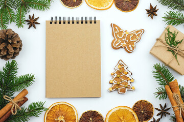 Christmas theme, gingerbread with glaze and notepad top view. New Year composition with cookies and fir branches. Christmas dinner menu writing. Pine cones, dry oranges, cinnamon and iced cookies.