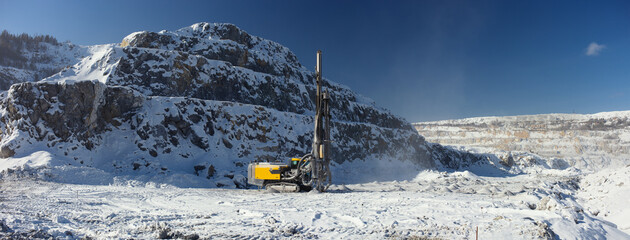 Mobile drilling machine against the background of rock wall in a snow-covered stone quarry in a...