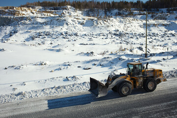 Wheeled front-end loader moves along the road in a snow-covered stone quarry, close-up.
