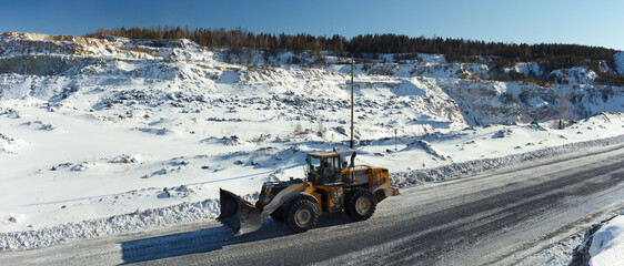 Wheeled front-end loader moves along the road in a snow-covered stone quarry, panorama. © esalienko