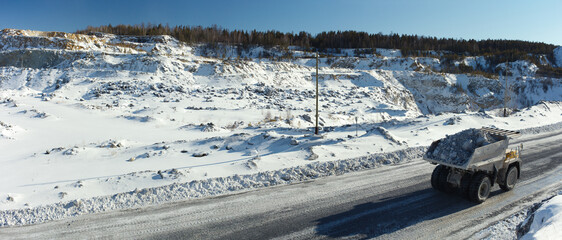 Heavy mining truck transports stone ore against the background of a snow-covered quarry in sunny...
