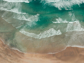 Aerial view turquoise waves slowly rolling onto an empty beach