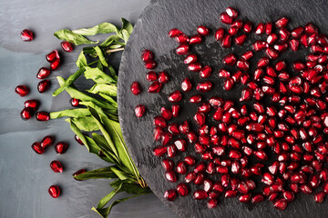 Scattered beautiful, juicy, ripe, red pomegranate seeds on a round stand of slate and pomegranate leaves on a black background