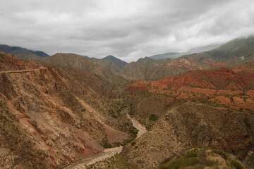 Geology. Panorama view of the red sandstone and rocky mountains, cliffs,  and river flowing across the valley under a cloudy sky in Miranda Slope, La Rioja Argentina.	