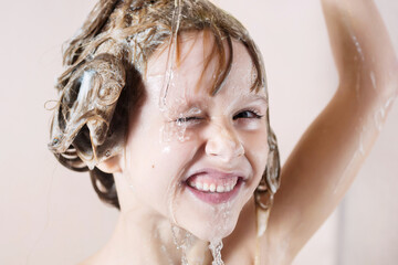 a little girl washes her hair with shampoo. water pours on her head and she closes her eyes and laughs. playing with water