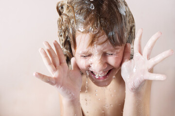 charming little blonde girl washes her hair in the bathroom with foam on her head. water pours, drops fly