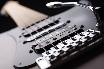 Fototapeta na wymiar Elegant electric guitar on black background close up point of view showing from bridge silver saddles and humbucker pickups to neck head with silver tremolo