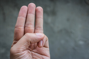 A young man showing his hands holding three fingers on a gray background.