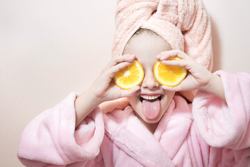 a little girl in a pink robe and a bath towel on her head covers her eyes with oranges on a pink background - Powered by Adobe