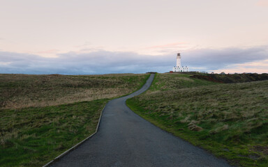 Fototapeta na wymiar Lighthouse under bright sky with grasses and road in foreground, Flamborough, UK.