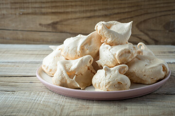 Homemade meringue cookies on a plate, on a wooden table by the window, closeup. Italian, French sweet dessert made of eggs and sugar, natural light.