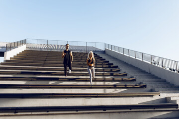 We work on the stairs. Sportive young couple in sportswear running together on stairs, outdoors