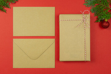 Christmas letter concept. Blank paper card, craft paper envelope, vintage gift box, rope, thuja branches on red background.Holiday Flat lay. Top view. Copy space. Mockup.