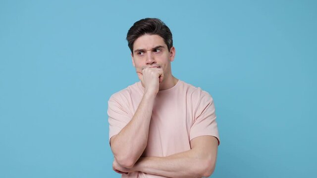 Confused puzzled young man 20s years old wearing casual beige t-shirt posing isolated on blue background in studio. People lifestyle concept. Looking camera spreading hands put hand prop up on chin