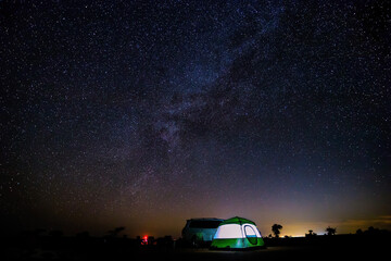 The car, tent, stars and the milkyway in the middle of a desert at night.