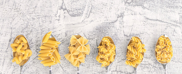 Banner with various pasta on spoons over white stone background. Top view with space for text.