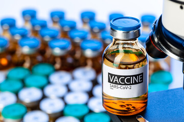 Vial of Covid-19 vaccine next to a microscope