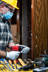 Carpenter worker at work repair and install a room door lock, wear the surgical mask to prevent Coronavirus infection. Preventing Pandemic Covid-19 at the workplace. Carpentry.