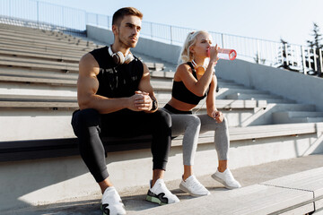 Young sportive couple in sportswear, taking a break to drink water, sitting on the stairs outdoors
