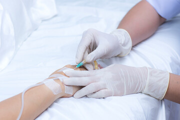 A nurse's hand gently pricks a medical needle into a sick patient's hand to prepare a saline solution and medicine for the debilitated patient