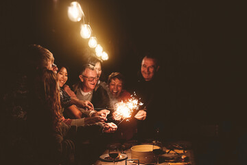 Happy family celebrating holidays with sparklers fireworks at night dinner party - Group of people...