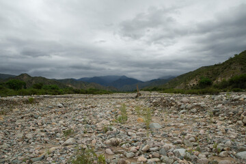 Hiking. Panorama view of the dried rocky river bed, mountains and forest under a cloudy sky in a summer day. 