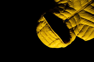 Yellow down jacket on black background. Quilted jacket perfect for winter. Close up.