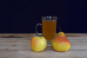 Apple, pear and glass with juice on a wooden table.