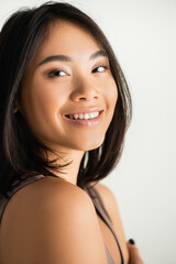 brunette asian woman smiling while looking at camera isolated on white