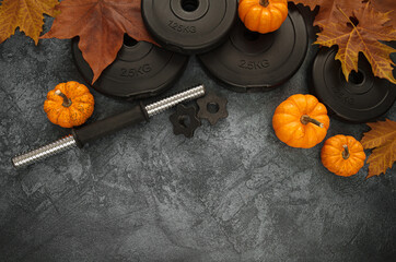 Heavy dumbbells weight plates, small decorative pumpkins and autumn leaves. Gym flat lay composition with copyspace, healthy fitness lifestyle fall concept.