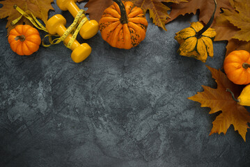 Two yellow dumbbells with tape measure (or measuring tape), small decorative pumpkins and autumn leaves. Gym flat lay composition with copyspace. Healthy fitness lifestyle fall concept.
