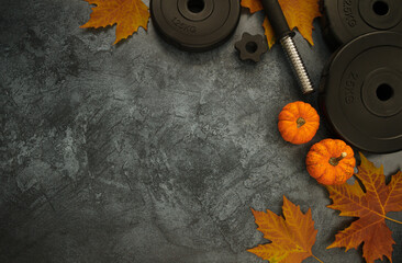 Heavy dumbbells weight plates with small decorative pumpkins and autumn leaves. Gym workout flat...