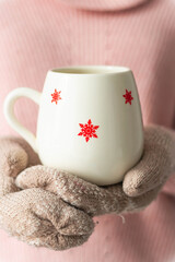 Girl holding cup with snowflakes close up on light background.Girl hands in teal gloves holding a mug with hot cocoa, tea or coffee. Winter and Christmas time concept.