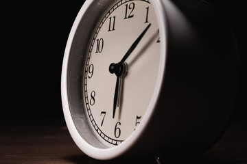 Vintage white alarm clock on a wooden table, with black background. Old retro analog twin bell...