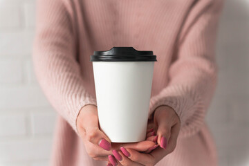 Girl holding white paper cup of takeaway coffee in the hand. Place for your text or log. Winter and Christmas time concept.