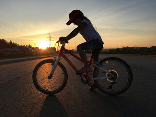 Obraz premium silhouette of a child in a cap on a bicycle and the glow of the sun