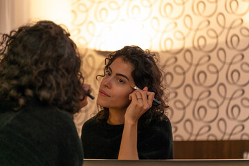 A brunette woman with curly hair in front of the mirror. Lifestyle. Fashion. Make-up