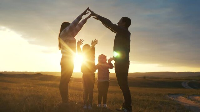 happy family. teamwork adult parents and small children shows a house and comfort symbol silhouette at sunset. happy family lifestyle mom dad and kids children portray a house roof hold their hands