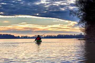 Woman kayaking on green kayak in winter Danube river at sunset. Back view. Concept: adventure, holiday, vacation