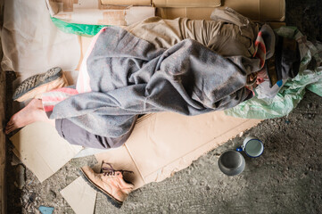 Top view of old homeless man wearing sweater and blanket sleeping on cardboard seeking help because hungry and food beggar from people walking pass on street.