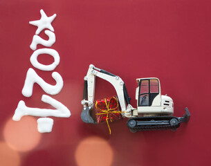 white model of toy metal excavator holding red mini gift, new year 2021 numbers on red background