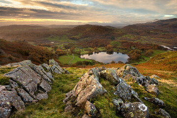 Aerial view of Loughrigg Tarn with rocks in foreground on a beautiful Autumn morning. Lake District, UK.