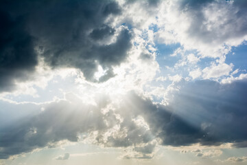 Beautiful dramatic sky with sun rays shining through dark clouds for background