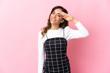 Young caucasian woman isolated on pink background saluting with hand with happy expression